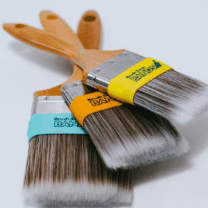 three Brush Saver Band reusable teal yellow and orange silicone sleeves that slide snugly over a paintbrush ferrule and upper bristles